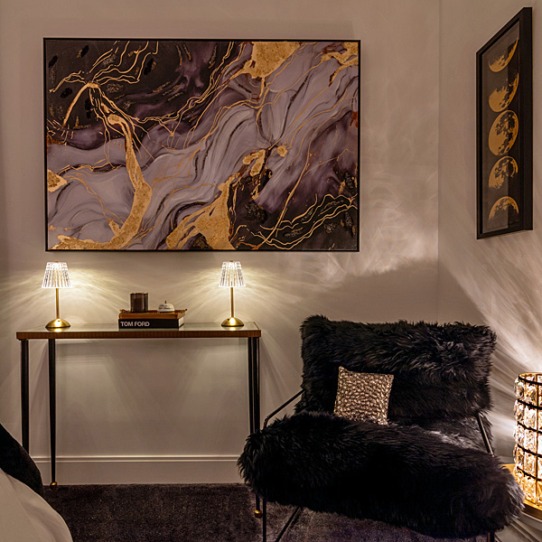 Lounge corner with gold-veined artwork, a crystal table lamp and a black shearling chair